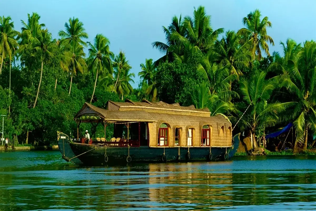 A traditional houseboat floating on the calm backwaters of Kerala with tropical palm trees in the background — best time to visit Kerala.
