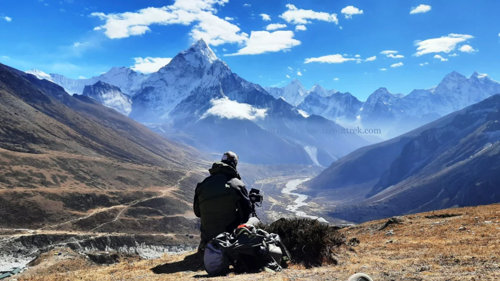 A trekker with a camera sitting on Singalila Ridge, admiring snow-covered Kanchenjunga — best time to visit Darjeeling for high-altitude trekking.