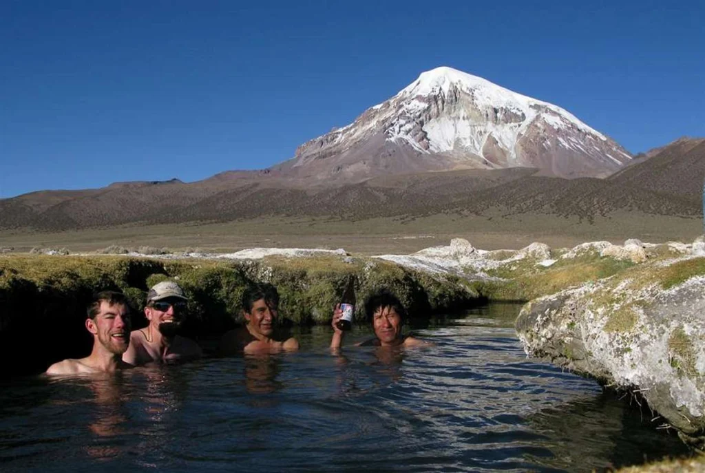 Traveler soaking in natural hot springs at Sajama National Park with snow-capped Andes in the background.